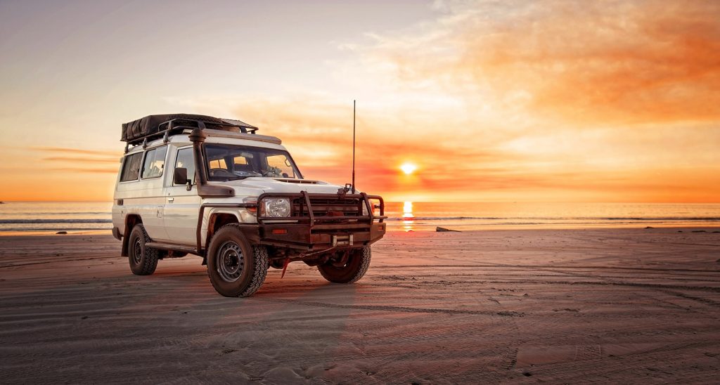 A 4WD driving on sand at sunset